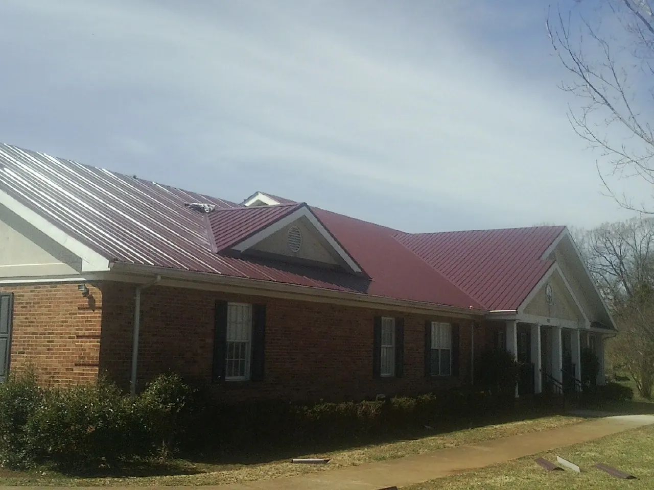 Red metal roof with gabled entries on a long brick building, from a Hail Damage Roof Repair job in Bernhards Bay
