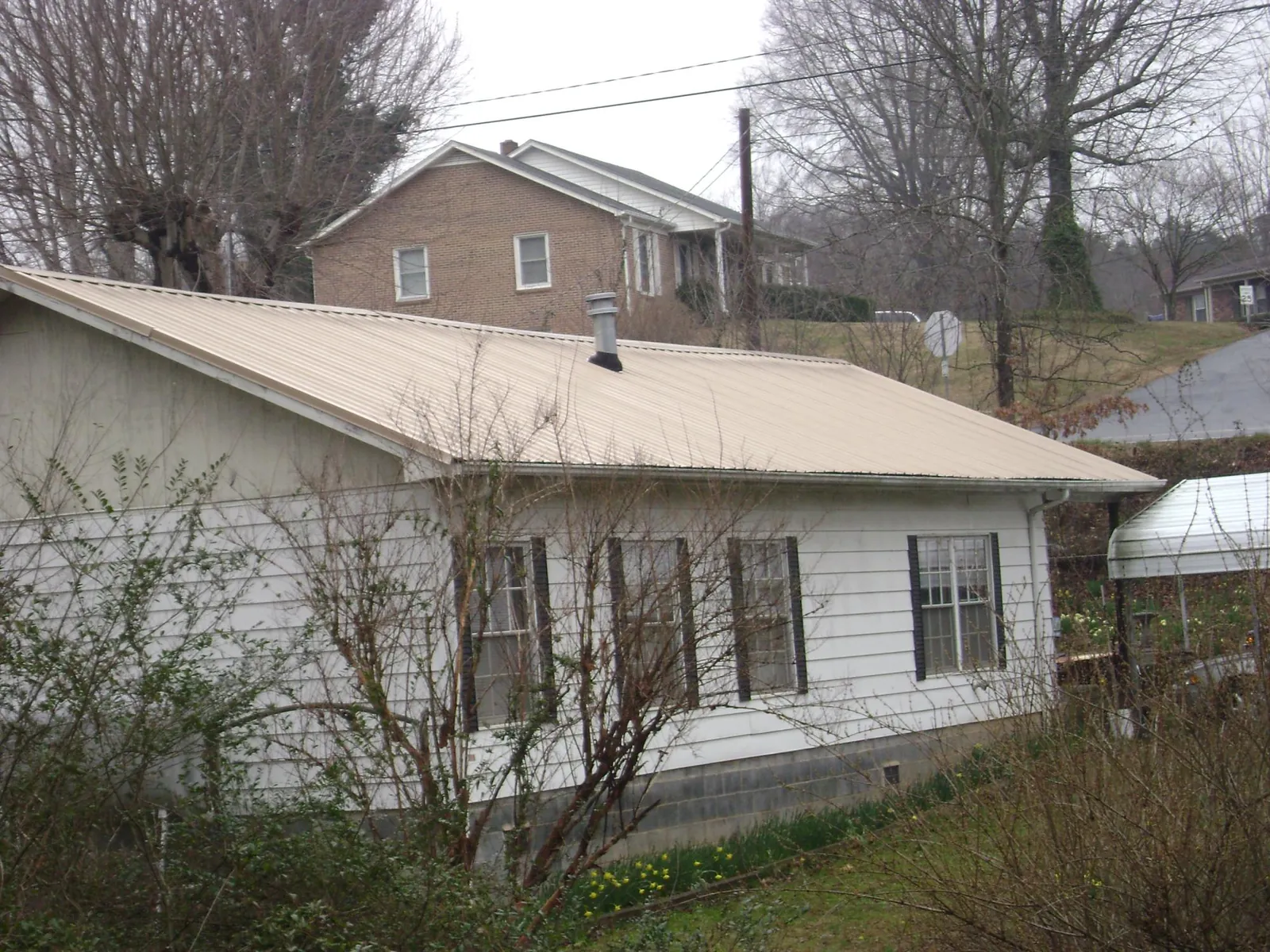Tan metal roof on a white sided house set into a hillside — Commercial Roofing by Roofing Brothers in Bernhards Bay